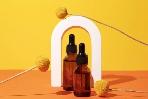 Two bottles different size with serum in arch with floral extracts craspedia Stock Photos