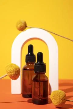 Two bottles different size with serum in arch with floral extracts craspedia Stock Photos