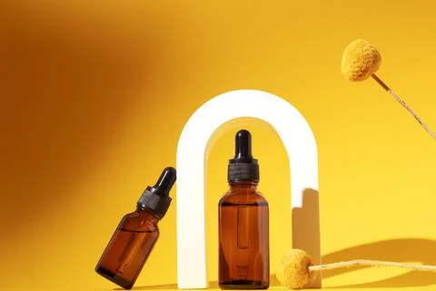 Two bottles different size with serum in arch with floral extracts craspedia Foto stock