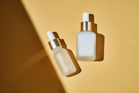 Two bottles of serum on a beige background with a beautiful shadow. Stock Photos