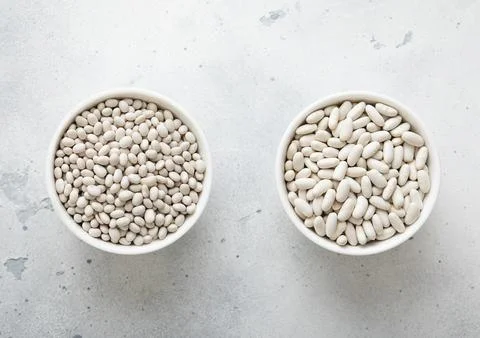 Two bowl plates with medium and small raw dry beans on kitchen table. Stock Photos