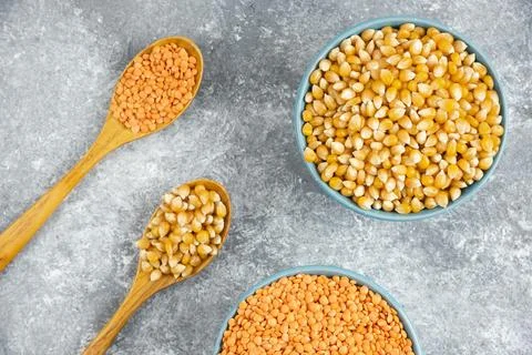 Two bowls of corn kernels and red lentil on marble surface Stock Photos