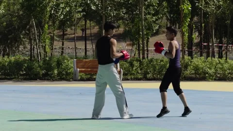 Two boxers facing each other in fighting stance outdoors during sunny training Stock Footage 318665762
