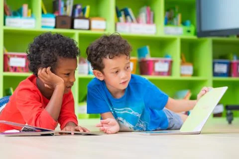 Two boy kid lay down on floor and reading tale book  in preschool library,Kin Foto stock