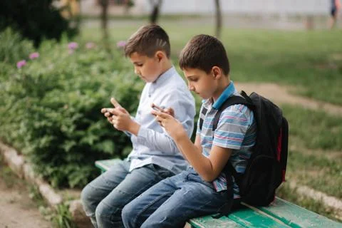 Two boy sitting on the bench and play online games. One boys with backpack Stockfoto's