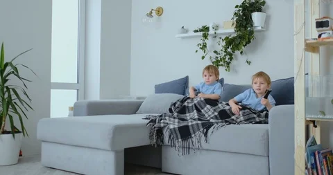 Two boys, 4 and 2 years old, are watching TV sitting on the couch. An exciting Stock Footage 105136998