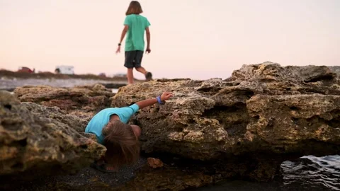 Two boys adeptly explore the rocky seaside, uncovering its secrets under the Stock Footage 250832218