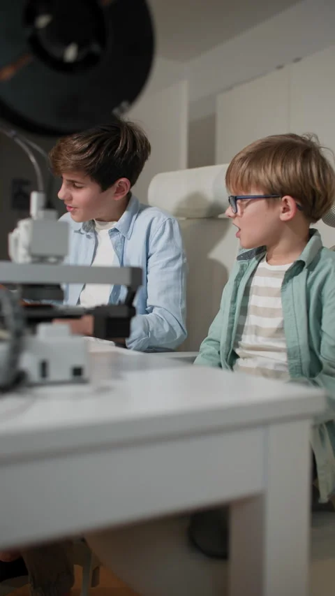 Two boys are chatting at a table, while 3D printer is working in the foreground Stock Footage 335390162