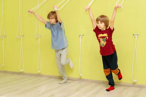 Two boys are doing exercises near a yellow wall with ropes. Stock Photos
