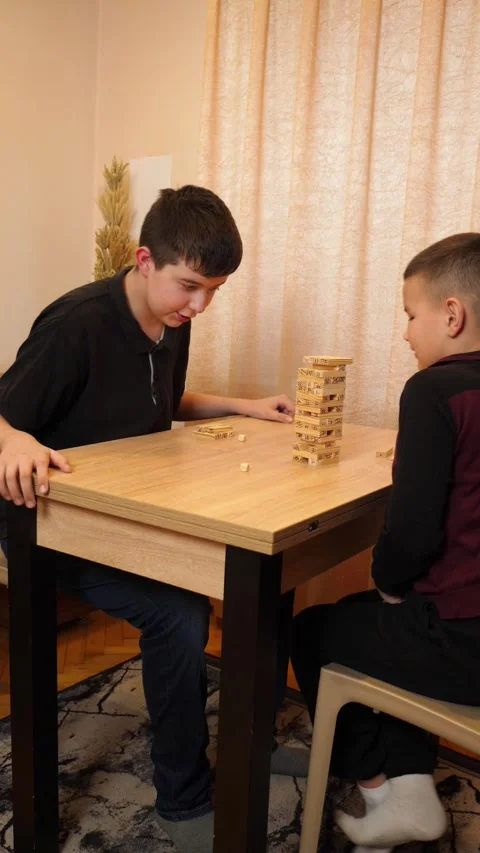 Two boys are playing a board game, building a pyramid out of wooden blocks. Stock Footage 313730224