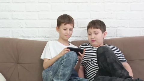 Two boys childs sitting on sofa, playing online game, smiling in light living Stock Footage 262779717