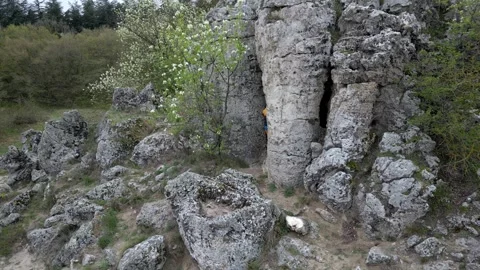 Two boys in colorful clothes explore a cave entrance among rugged rocks and Stock Footage 307592418