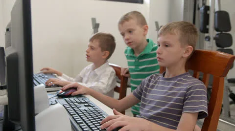 Two boys on computers as another boy looks on smiling Video stock 22569800