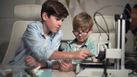 Two boys of different ages are sitting at table.They are monitoring 3D printer Stock Footage 335375505
