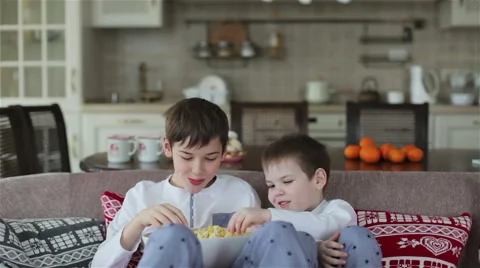 Two boys eating popcorn on a sofa in the dining room Video stock 58513161