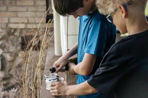Two boys engaged in a science experiment outdoors, one pouring liquid into .. Stock Photos