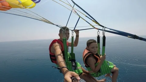 Two boys go parashuting after a motorboat pulling them over a sea coast 動画素材 84132616