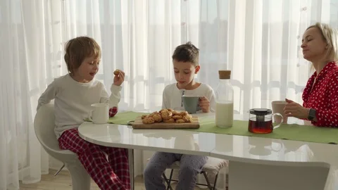 Two boys having breakfast in modern kitchen. Boy eat cookie with milk. White Video stock 103688318