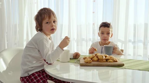 Two boys having breakfast in modern kitchen. Boy eat cookie with milk. White Stock Footage 103690666