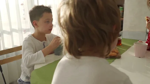 Two boys having breakfast in modern kitchen. Boy eat cookie with milk. White Video stock 103691147