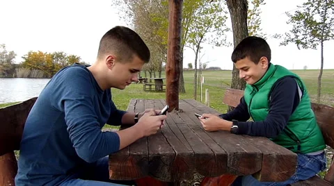 Two boys having fun with their smartphones on lake shore Stock Footage 44731132