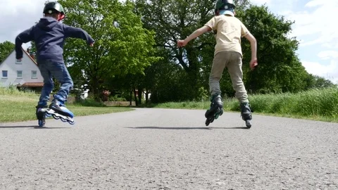 Two boys in helmets learning to drive roller skates in summer - 4 k Stock Footage 76823979