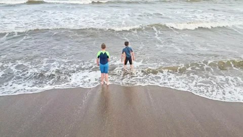 Two boys, joyfully playing in the sea, waves splashing on the shoreline Stockbeeldmateriaal 245931937