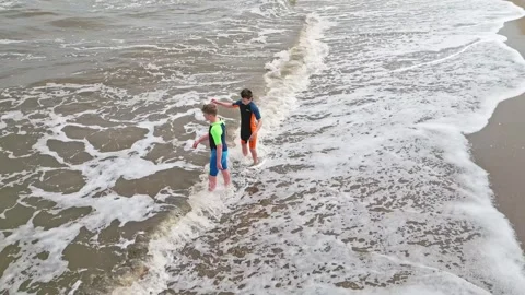 Two boys, joyfully playing in the sea, waves splashing on the shoreline Видео 245931985