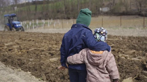 Two boys look how tractor cultivates the land for planting of the earth Stock-Footage 128531413
