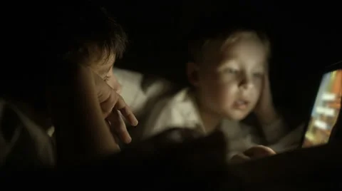 Two boys lying in bed at night and using pad Stock Footage 46195451