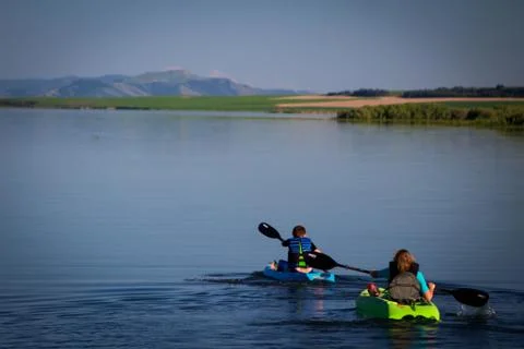 Two boys paddling kayaks in peaceful lake Stock Photos