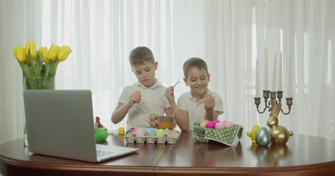 Two boys paint Easter eggs and greet each other. on the table is a computer that Stock Footage 176530068