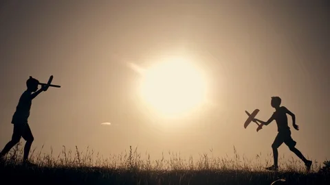 Two boys with a plane in their hands run across a green field in the rays of the Stock Footage 109215735