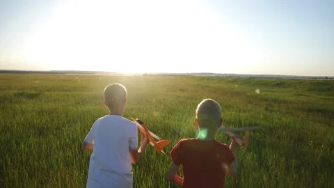 Two boys with a plane in their hands run across a green field in the rays of the Stock Footage 111616908