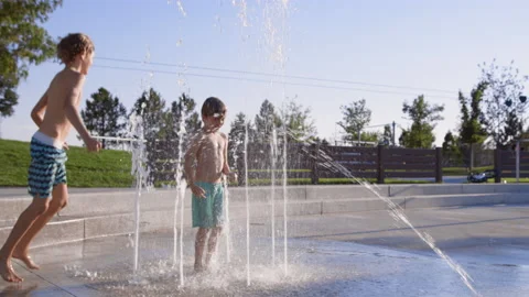 Two boys play together in splash pad, dancing around on summer afternoon Stock-Footage 233938892