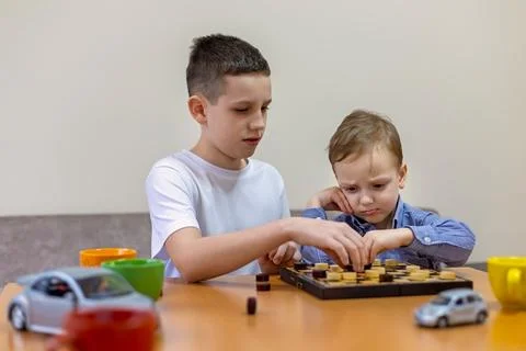 Two boys playing checkers at a table, with the younger one looking disappointed Stock-Fotos