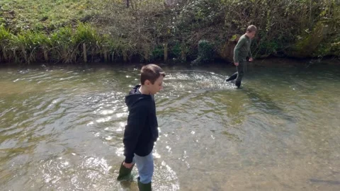 Two boys playing in a shallow stream. Walking in the river slowly together. 库存影片 240302266