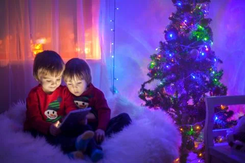 Two boys, playing on tablet at home, next to christmas tree Stock Photos
