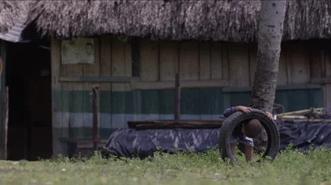 Two boys playing with tire outside a hut in village, Guatemala Stock Footage 63053780