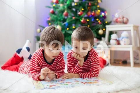 Two boys, reading a book in front of Christmas tree Stock Photos