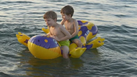 Two boys ride a bright inflatable at sea, laughing as gentle waves rock them Stock-Footage 318294290