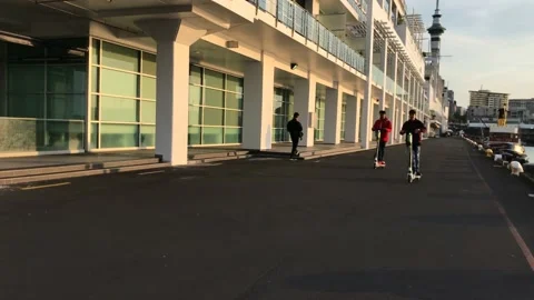 Two boys ride on scooters around the Auckland wharf Video stock 184328761