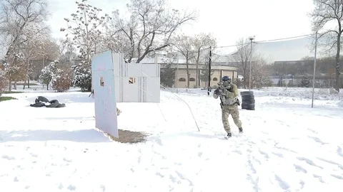 Two boys run and play airsoft. The player is in the snow, and fired from Stock Footage 72981097