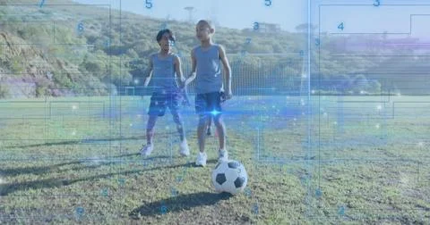 Two boys scanning digital data overlays on grassy center field, with soccer ball Stock Photos