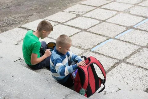 Two boys sit on concrete steps outside. One wears a green shirt and uses an e Stock Photos