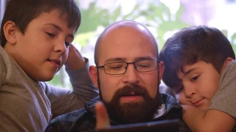 Two boys sit with their dad and watch him use his phone Vídeos de archivo 70724122
