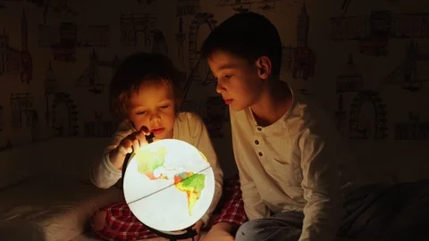 Two boys sitting in bed at night rotating the globe and dreams of traveling. Video stock 101042775