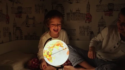 Two boys sitting in bed at night rotating the globe and dreams of traveling. Stock Footage 101043384
