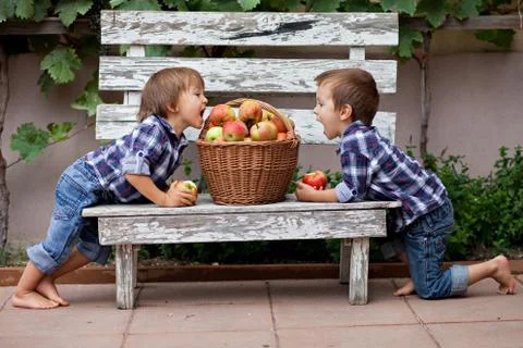Two boys, sitting on a bench, eating apples and having fun Stock Photos