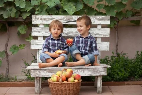Two boys, sitting on a bench, eating apples and having fun Stock Photos